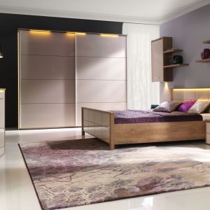 Sypialnia Wien to modne połączenie bieli na wysoki połysk z ciepłym drewnem. Intrygującym elementem w kolekcji jest oświetlenie komody, szafy czy wezgłowia łóżka. Fot. Stolwit