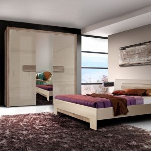 Sypialnia Tiziano ma jasne, ciepłe kolory, które doskonale nadają się do aranżacji przytulnej sypialni. Wąskie i wysokie lustro pomiędzy drzwiami w szafie  optycznie powiększy pokój. Fot. Meble Forte