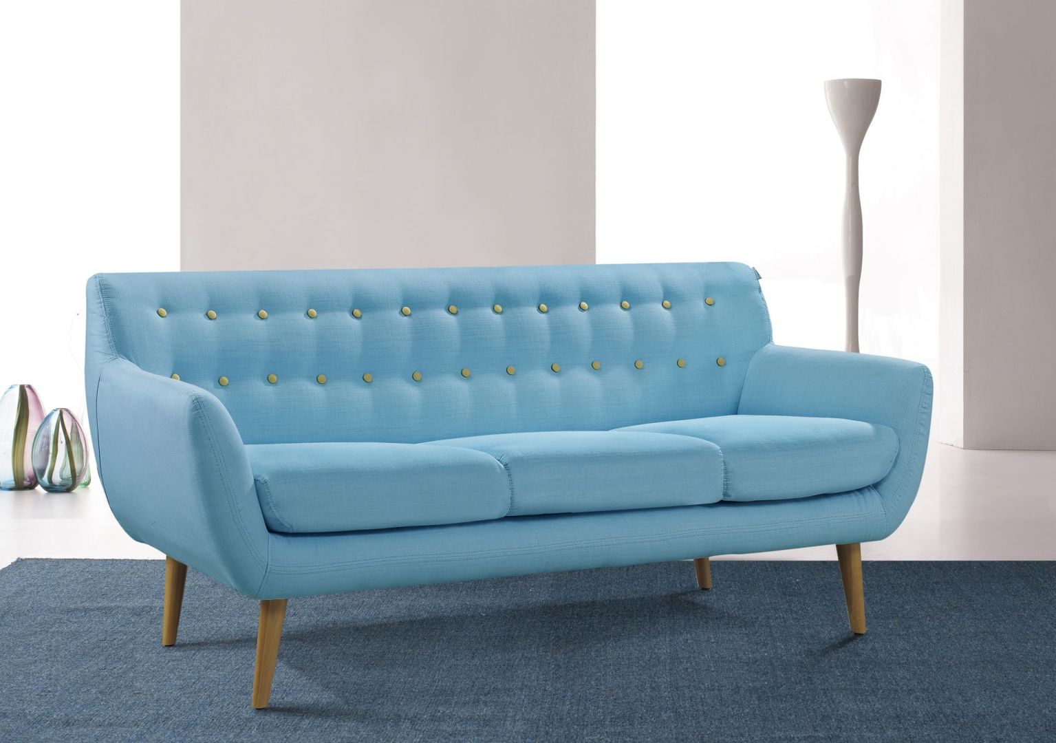 Ta trzyosobowa sofa z oryginalnym pikowaniem na oparciu to oryginalny projekt. Drewniane wysokie nóżki pięknie kontrastują z niebieską tkaniną. Sofa Sixty Design. Fot. Cranmore Home