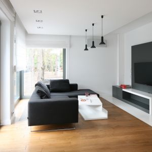 Szary panel telewizyjny na białej ścianie prezentuje się minimalistycznie. Dopasowano do niego szarą sofę. Projekt: Kasia Kiełek Fot. Bartosz Jarosz 