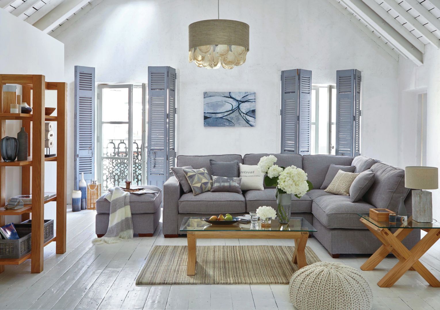 We wnętrzach w stylu marinistycznym oprócz bieli i błękitów nie może zabraknąć naturalnego drewna. Sofa w szarym kolorze doskonale współgra ze stolikiem na drewnianych nogach, o szklanym blacie. Fot. Dunelm