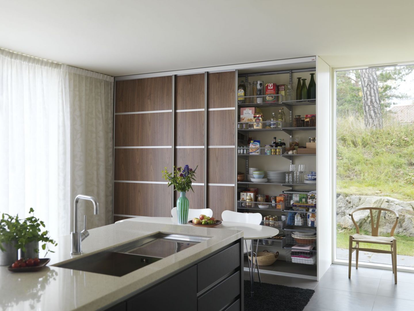 Drzwi przesuwne sprawiają, że wnętrze kuchni jest uporządkowane i minimalistyczne. Taka kuchenna szafa jest doskonałą alternatywą dla klasycznych szafek, jeśli chcesz urządzić kuchnię nowocześnie. Fot. Elfa