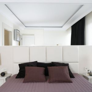 Białe panele niemalże zlewają się ze ścianą, a lustro nad łóżkiem optycznie powiększa przestrzeń. Projekt: Katarzyna Uszok. Fot. Bartosz Jarosz