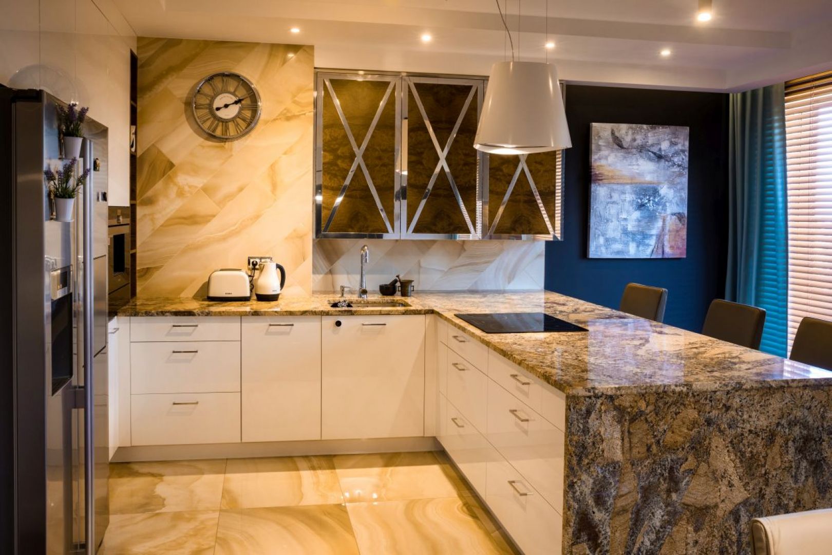 Mieszkanie zaprojektowane przez Viva Design W prostej, białej zabudowie kuchennej wykonanej przez stolarza pojawiły się szafki z dekoracyjnym fornirem zdobionym chromowanymi listwami.