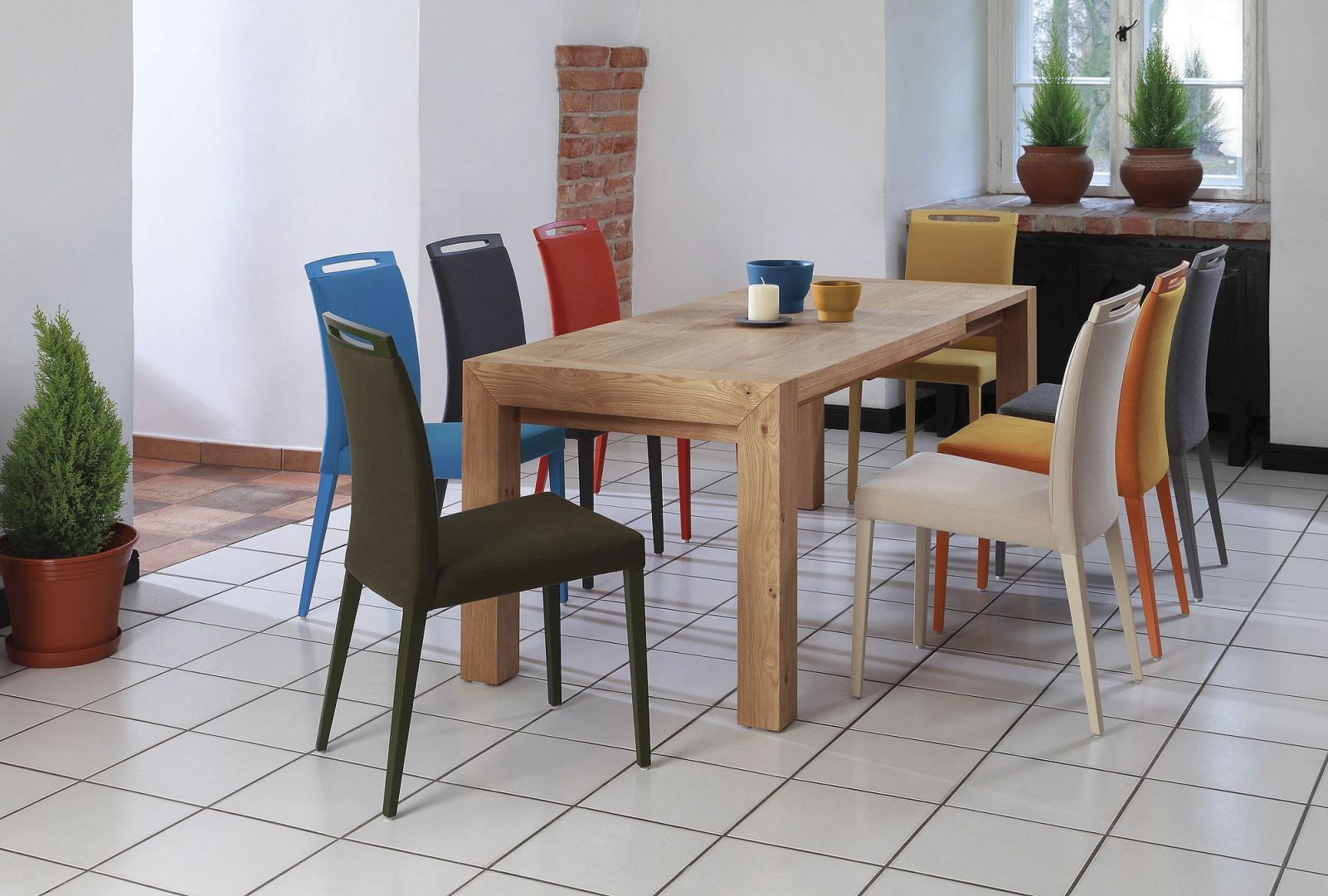 Do prostego drewnianego stołu pasują kolorowe tapicerowane krzesła. Fot. Klose