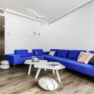 Błękitna sofa w połączeniu z drewnianą podłogą i białymi ścianami podkreśla marynistyczny klimat salonu. Projekt Paulina Kasprowicz