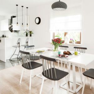 W jadalni do dużego białego stołu dopasowano bukowe krzesła-patyczaki na białych nogach z czarno-szarym siedziskiem i oparciem. Projekt: Kinga Świątek-Wolna. Fot,. Make Home