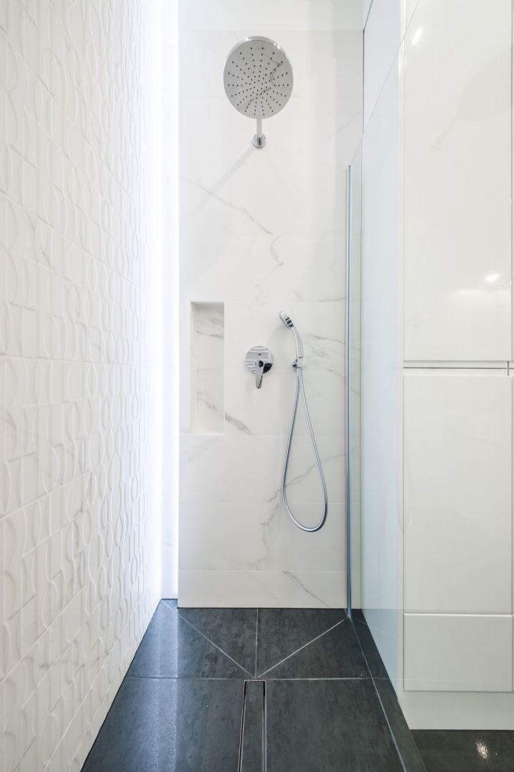Mariaż elegancji z nowoczesnością znajdziemy również w łazience, gdzie drewno i marmur spotykają się ze szkłem, punktowym oświetleniem i gładką powierzchnią frontów meblowych. Projekt: Kodo. Fot. Kodo
