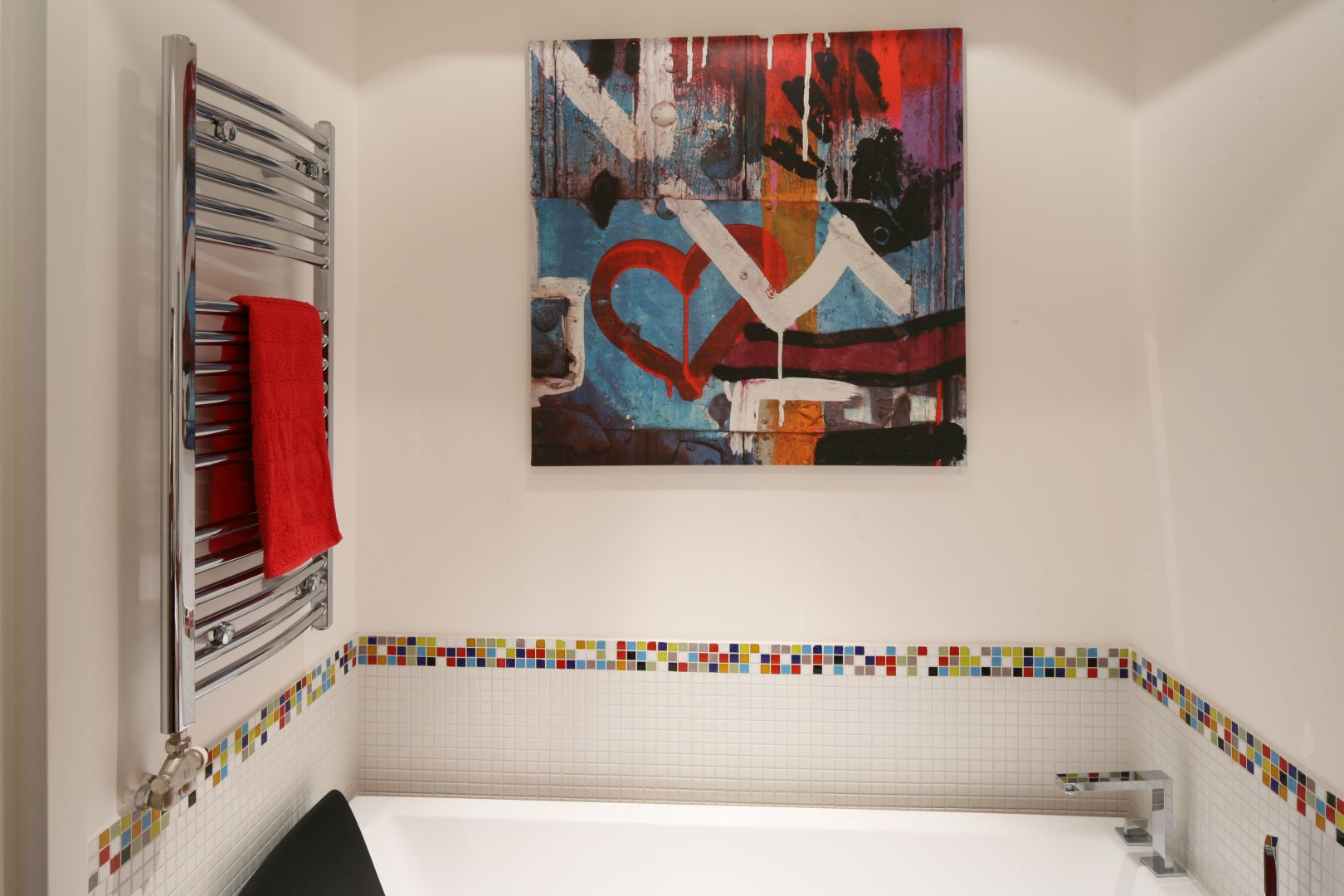 Ścianę nad wanną chroni przed zachlapaniem mozaika. Do jej kolorowej bordiury, której inspiracją była kostka Rubika, dopasowano obraz powyżej oraz czerwone dodatki. Fot. Bartosz Jarosz