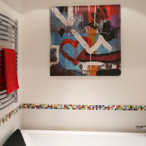 Ścianę nad wanną chroni przed zachlapaniem mozaika. Do jej kolorowej bordiury, której inspiracją była kostka Rubika, dopasowano obraz powyżej oraz czerwone dodatki. Fot. Bartosz Jarosz