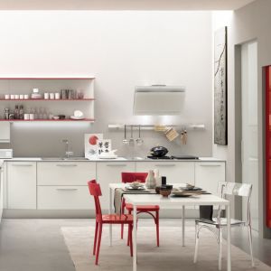 Białą zabudowę kuchni Alicante marki Febal Casa ożywiają czerwone akcenty. Ta swoista gra bieli i czerwieni została podkreślona poprzez kolor stołu i krzeseł w mini jadalni. Fot. Febal Casa.