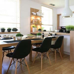 Przestronna jadalnia została połączona z kuchnią. Jej centrum stanowi duży, masywny stół, który zdobią designerskie krzesła. Urządzona w jasnym drewnie wizualnie ociepla białą kuchnię. Projekt Małgorzata Błaszczak. Fot. Bartosz Jarosz.