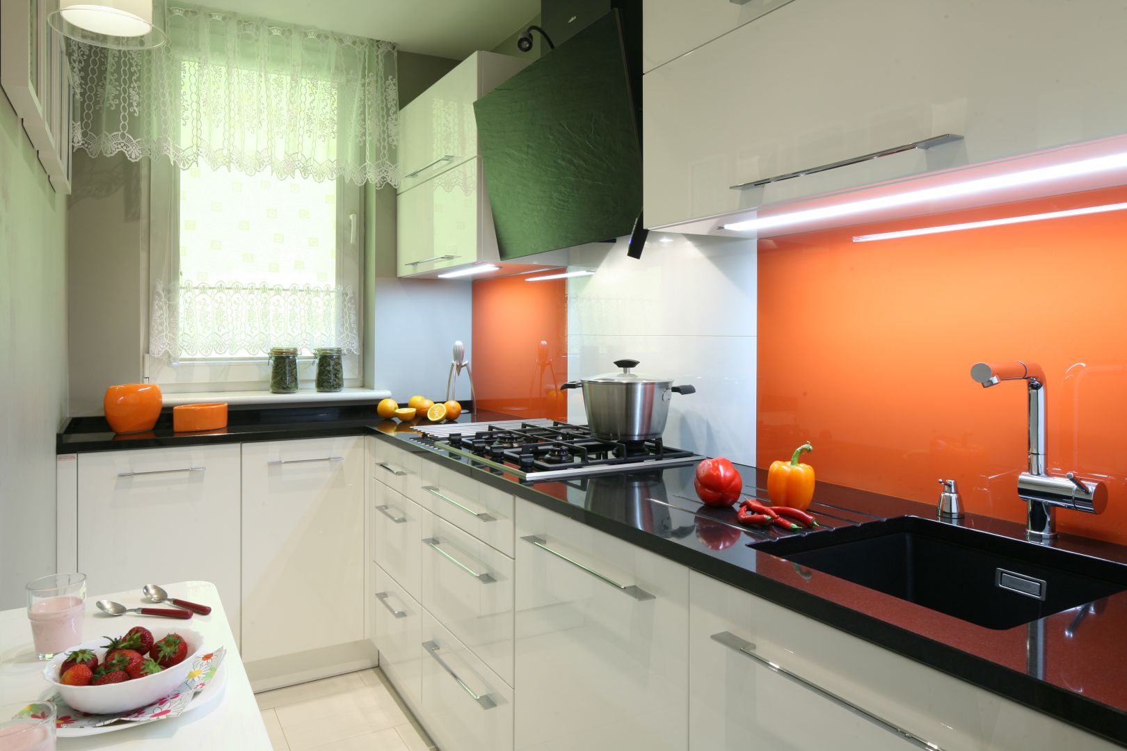 Wąską zamkniętą kuchnię urządzono niezwykle praktycznie, a przy tym elegancko. Kolor pomarańczy efektownie ożywił białą aranżację. Projekt Studio Śląskie Kuchnie. Fot. Bartosz Jarosz.