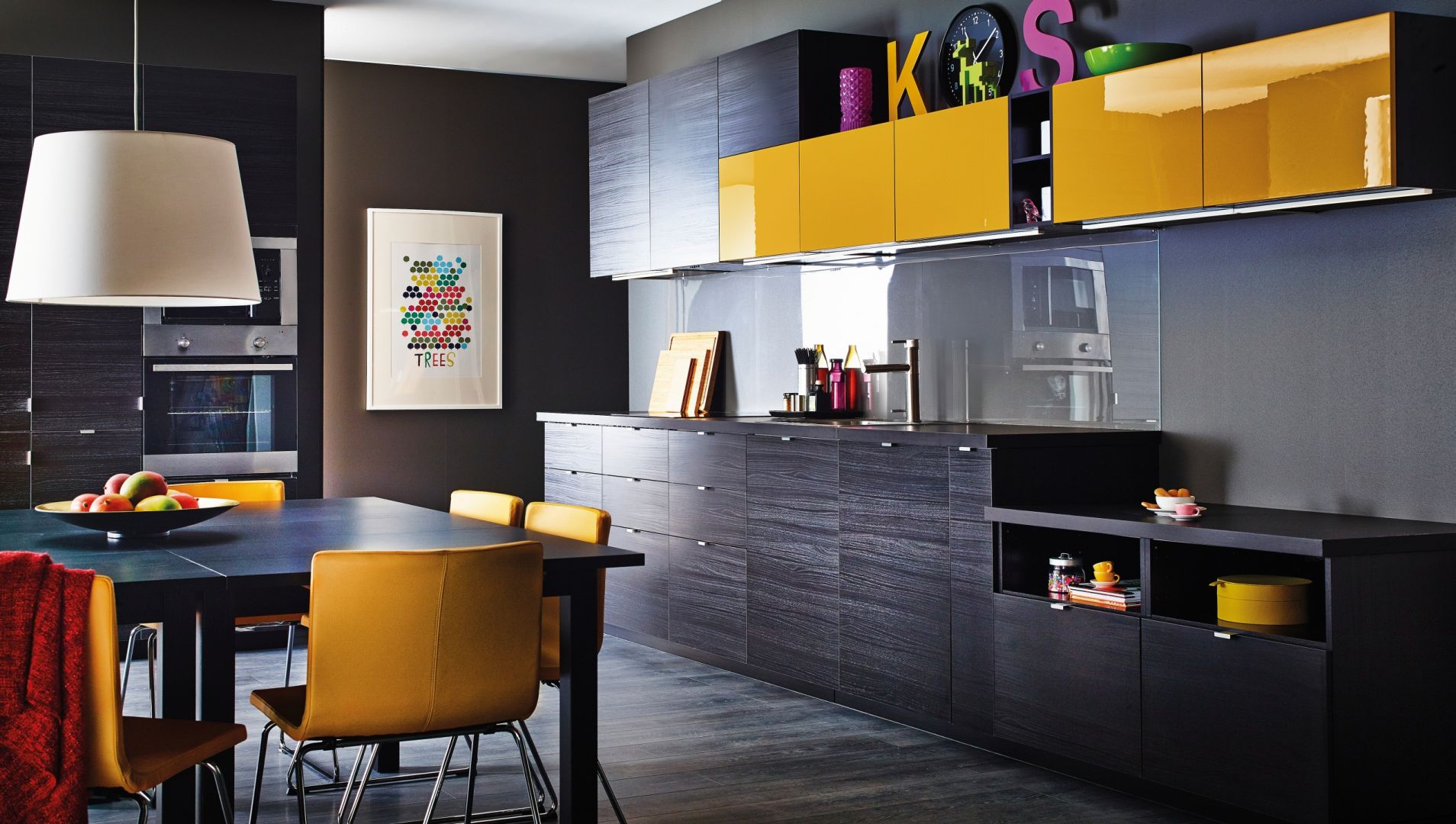 Na zdjęciu: kuchnia Metod firmy IKEA; ściana wykończona przezroczystym szkłem podkreśla ciekawą kolorystykę mebli – imitującą czarne drewno oraz żółty w połysku. Fot. IKEA.