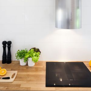 Strefę gotowania wyróżnia nowoczesny okap z podświetleniem. Na blatach położono naturalny dąb – materiał, który w roli akcentu pojawia się w całym domu.