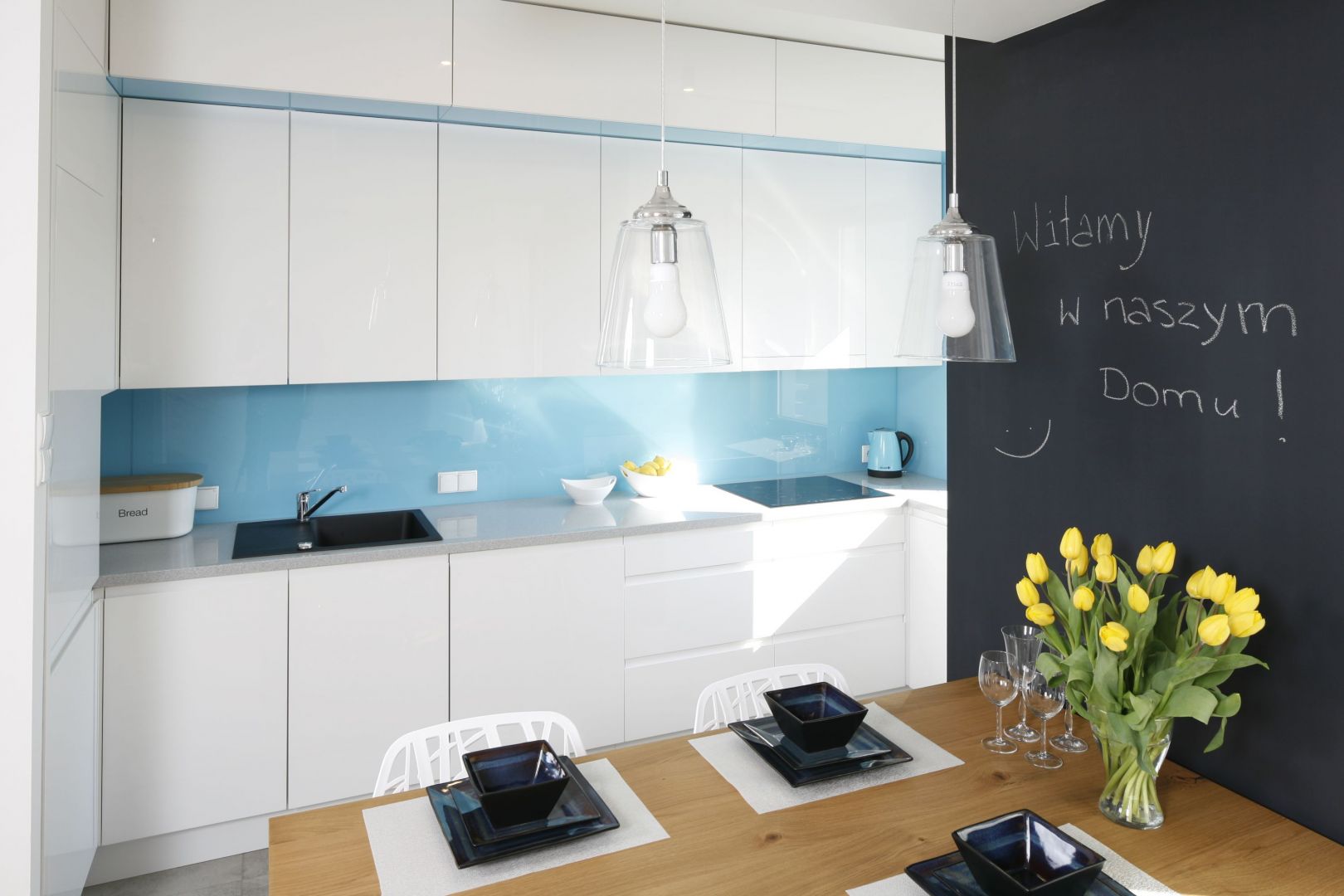 W białej kuchni postawiono na niebieskie szkło na ścianie nad blatem. Projekt Agnieszka Zaremba, Magdalena Kostrzewa-Świątek. Fot. Bartosz Jarosz.