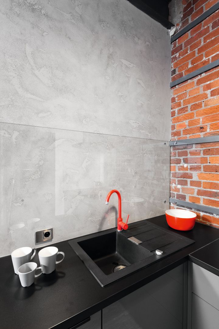 W aranżacji mieszkania przewija się czerwień, przełamująca monotonię szarych ścian. Kolor ten powtórzono również w kuchni, w postaci stylowej baterii, która ożywiła strefę zmywania.