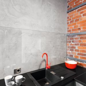 W aranżacji mieszkania przewija się czerwień, przełamująca monotonię szarych ścian. Kolor ten powtórzono również w kuchni, w postaci stylowej baterii, która ożywiła strefę zmywania.