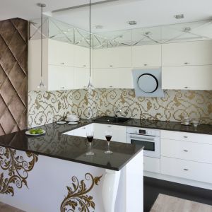 Białą zabudowę kuchenną zdobią liczne detale w stylu glamour, w tym złota mozaika, której klasyczny wzór powtórzono na frontach wyspy. Projekt Agnieszka Hajdas-Obajtek. Fot. Bartosz Jarosz.