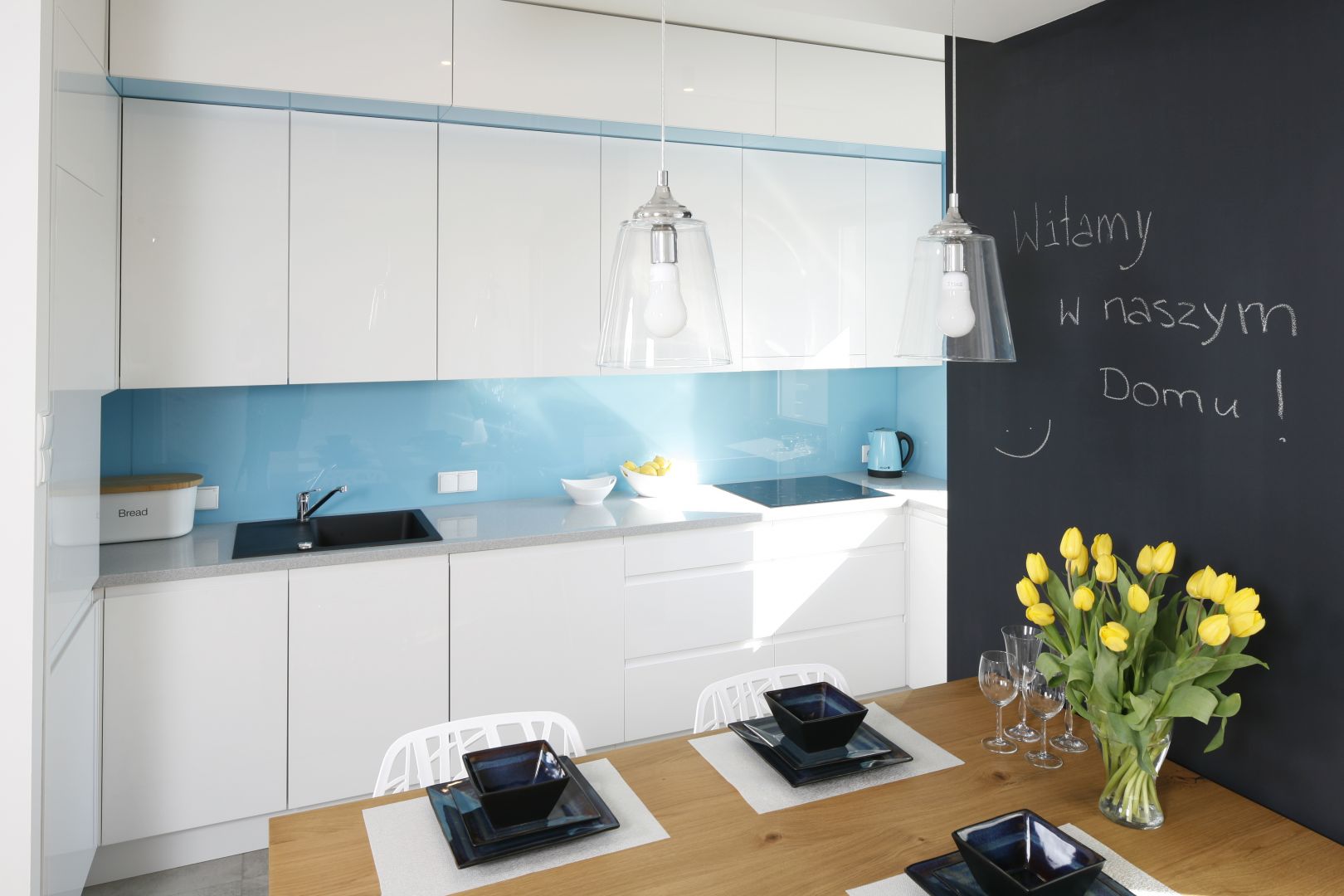 W białej kuchni zdecydowano się na niebieskie szkło na ścianę nad blatem. Projekt Agnieszka Zaremba, Magdalena Kostrzewa-Świątek. Fot. Bartosz Jarosz.