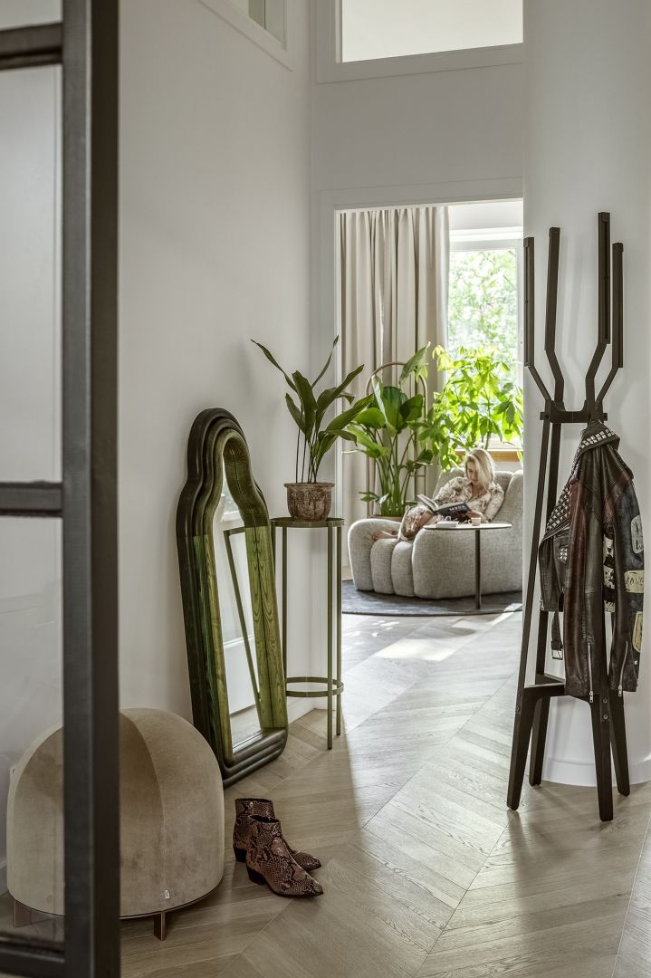 Beżowa pufa Stado (Nurt), lustro TRN mirror/triple (Pani Jurek), drewniany wieszak Pilo (Tfory), kwietnik Blossom (The Good Living & Co), rośliny (Plants For Humans), fotel projektu Tomka Rygalika (Nobonobo).
