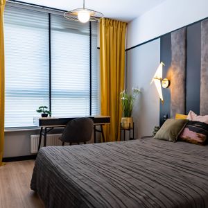 W sypialni, sprytnie ukrytej za ścianą z fototapetą, dominuje szara kolorystyka ścian i zagłówka, ocieplona żółtymi dodatkami. Projekt: DG Studio Donata Gadalska. Fot. Jacek Fabiszewski