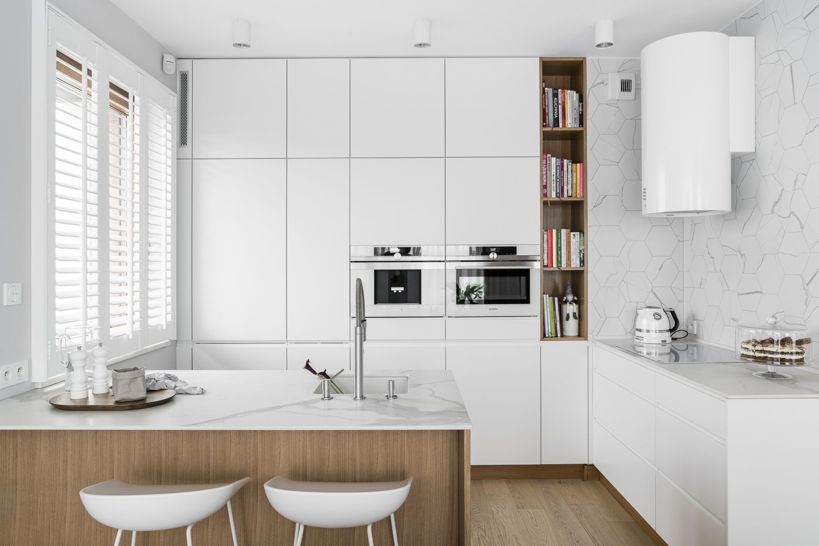 Białą kuchnię połączono z subtelnie wprowadzanymi dekorami drewna i marmuru. Projekt Maka Studio