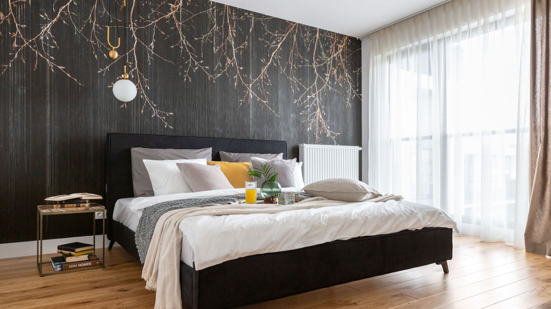 Biel i drewno dobrze komponują się z tapetą wpadającą w grafit z motywem złotych gałązek, która zdobi ścianę za łóżkiem. Projekt: Decoroom. Fot. Marta Behling, Pion Poziom