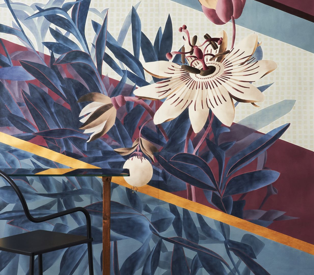„Passiflora”, czyli kwiat męczennicy z owocami, jest niekwestionowanym bohaterem tej tapety. Ponadwymiarowy design łączy się tu z bujną paprocią poprzez naprzemienne nakładanie się i przenikanie elementów poszczególnych planów.
Inspiracją dla tła jest świat tekstyliów, gdzie geometryczne mikro wzory występują naprzemiennie z szerokimi ukośnymi paskami. Na jej wyjątkowy wygląd wpływają dodatkowo ręcznie haftowane detale, które nadają kwiatom aspekt pełnej trójwymiarowości. Fot. Mood-Design