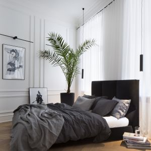 W sypialni właścicielki znajduje się duże łóżko z eleganckim wezgłowiem w intensywnej czerni, które świetnie kontrastuje z bielą ścian ozdobionych dekoracyjnymi listwami oraz długimi jasnymi zasłonami. Projekt Goszczdesign. Fot. Piotr Mastalerz 