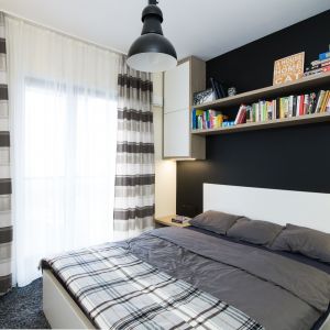 Ścianę za łóżkiem wykończono czarną farbą. Kontrastem są białe szafki i drewniana półka na książki. Projekt i zdjęcia: Joanna Nawrocka