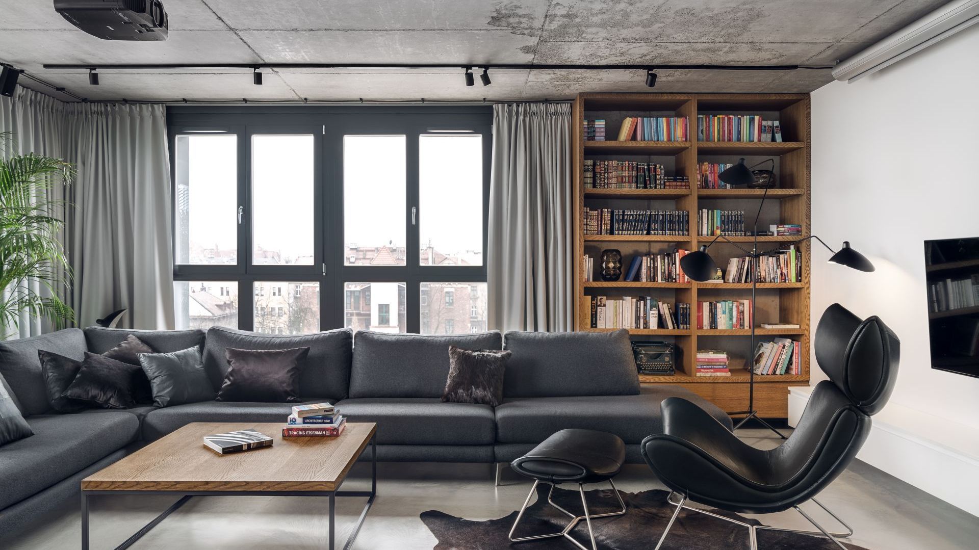 Drewniana otwarta szafa na ścianie za kanapą zapewnia spora ilość miejsc na domową biblioteczkę. Projekt: BLACKHAUS Karol Ciepliński Architekt. Fot. Tom Kurek