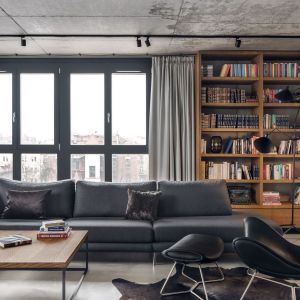 Drewniana otwarta szafa na ścianie za kanapą zapewnia spora ilość miejsc na domową biblioteczkę. Projekt: BLACKHAUS Karol Ciepliński Architekt. Fot. Tom Kurek