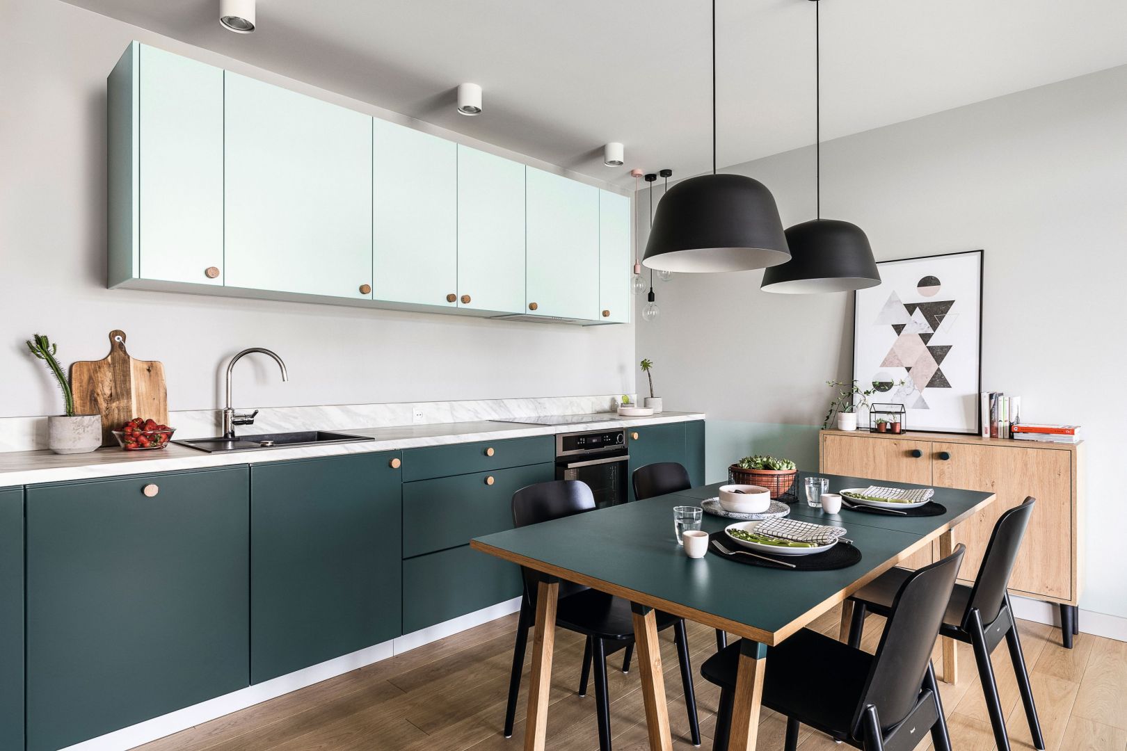 Ta kuchnia z dolnymi frontami w głębokim malachitowym odcieniu pięknie komponuje się ze stołem w jadalni i otwartą częścią dzienną. Projekt Raca Architekci. Fot. Fotomohito
