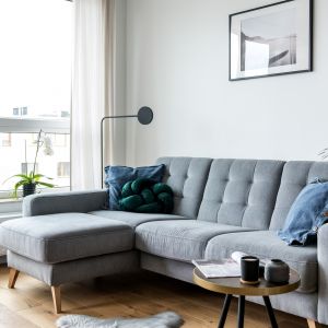 Szara sofa z charakterystycznym pikowaniem nadaje niedużemu salonowi stylowy wygląd. Projekt Deer Design