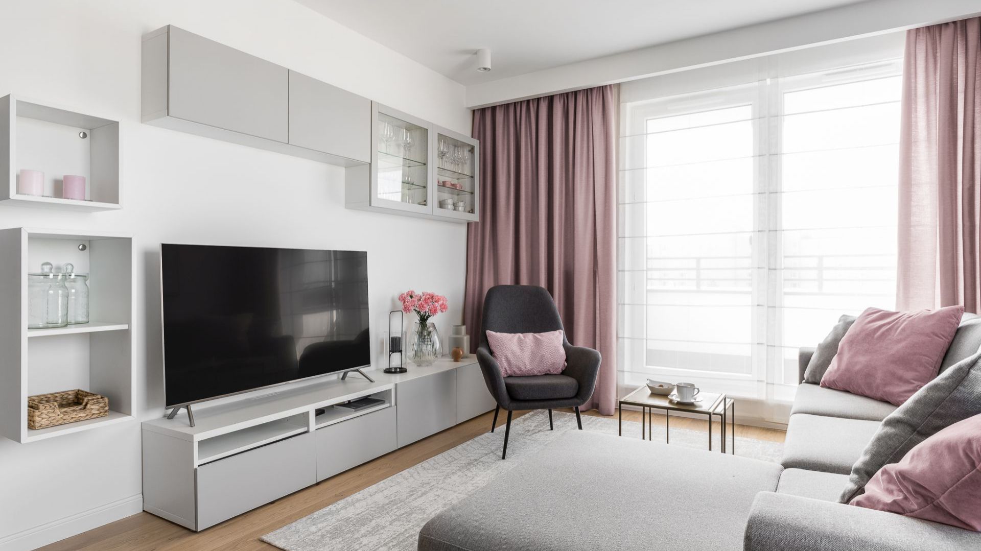 Nowoczesny jasny salon w bloku. Biała zabudowa na ścianie telewizyjnej, prosta szara sofa i kolor w dodatkach. Projekt: Barbara Wojsz. Fot. Fotomohito