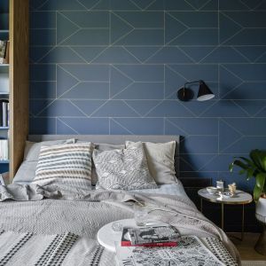 Ściana za łóżkiem w sypialni wykończona jest ciemną, niebieską tapetą o delikatnym geometrycznym wzorze. Projekt: Magdalena Bielicka, Maria Zrzelska-Pawlak, pracownia Magma. Fot. Kroniki Studio