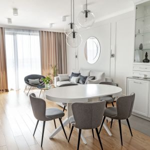 Jasnoszare ściany, białe meble i drewniana podłoga podkreślają spójność wystroju części dziennej. Projekt: Studio Projektowania Miśkiewicz Design. Fot. Anna Powałowska