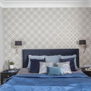 Ściana za łóżkiem w sypialni wykończona jest klasyczną tapetą w biało-szarym kolorze. Projekt: Decoroom. Fot. Pion Poziom