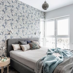 Ściana za łóżkiem w sypialni wykończona jest tapetą inspirowana naturą. Jej chłodna kolorystyka świetnie pasuje do szarego, tapicerowanego łóżka. Projekt Magdalena Bielicka, Maria Zrzelska-Pawlak, pracownia Magma. Fot. Fotomohito