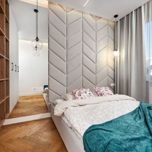 Ścianą za łóżkiem wykończona jest  tapicerowanym zagłówkiem w jasnym, szarym kolorze. Projekt: Kornelia Knapik Ziemnicka, Kora Design. Fot. Marek Królikowski