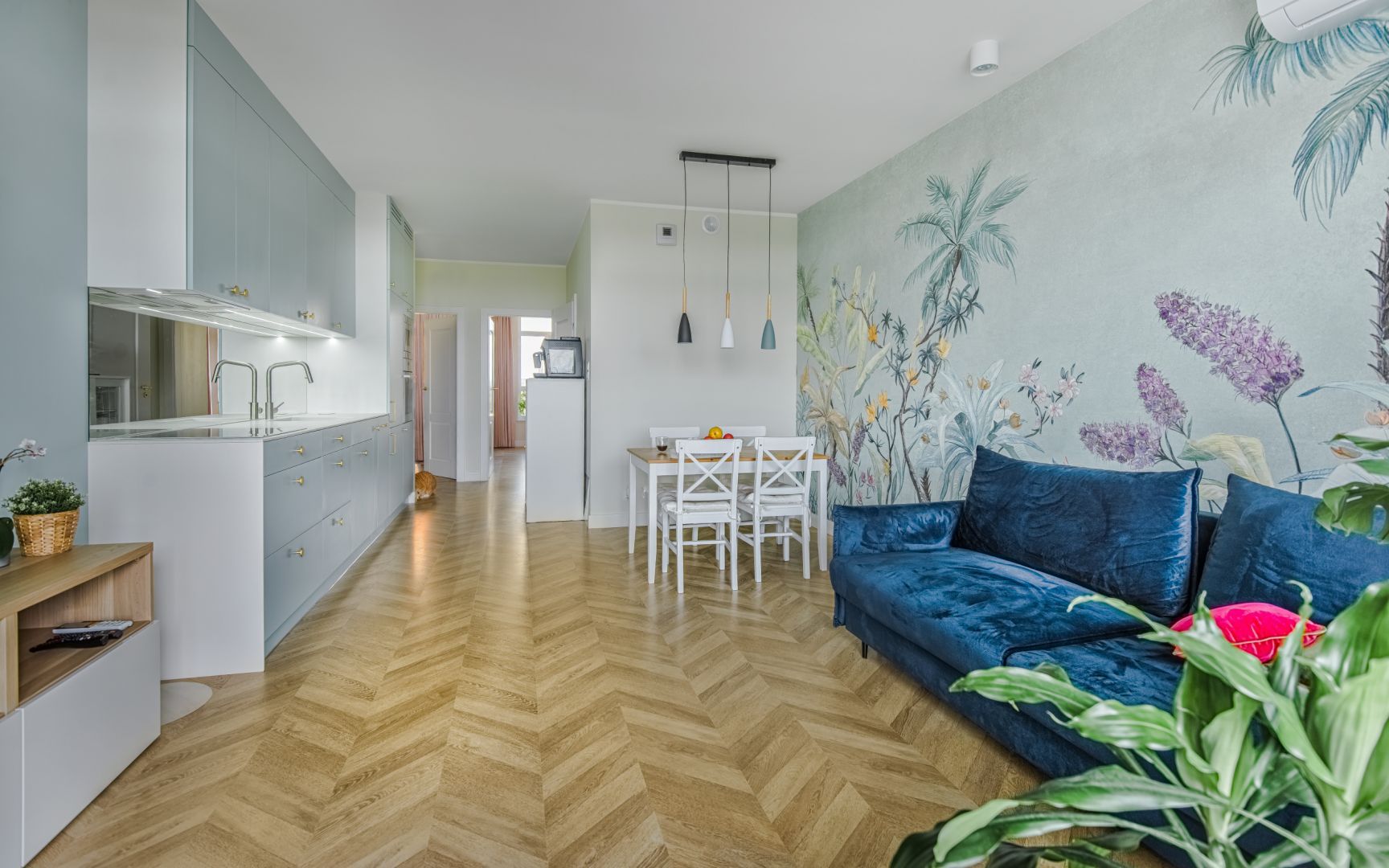 Mały salon połączony z kuchnią i jadalnią urządzono w jasnych kolorach. Podłogę wykończono drewnem ułożonym w elegancką jodełkę. Projekt: Beata Ignasiak, pracownia Ignasiak Interiors. Fot. Grupa Deix