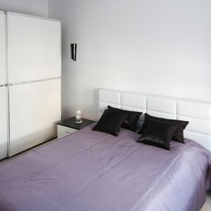 Białą szafę z drzwiami przesuwnymi ustawiono w sypialni równolegle do łóżka. Projekt: Joanna Ochota. Fot. Bartosz Jarosz