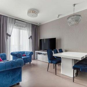 Niebieski fotel i kanapa z dekoracyjnymi pikowania pięknie pasują do jasnych kolorów zastosowanych w salonie. Projekt: Beata Ignasiak, pracownia Ignasiak Interiors. Fot. Grupa Deix