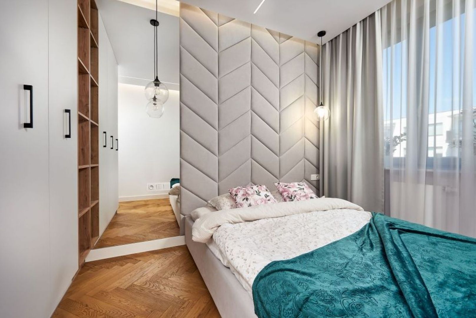 Ścianą za łóżkiem w małej sypialni pięknie zdobi tapicerowany zagłówek w jasnym, szarym kolorze, powiększają zaś duże lustra. Projekt: Kornelia Knapik Ziemnicka, Kora Design. Zdjęcie: Marek Królikowski