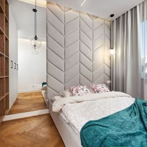 Ścianą za łóżkiem w małej sypialni pięknie zdobi tapicerowany zagłówek w jasnym, szarym kolorze, powiększają zaś duże lustra. Projekt: Kornelia Knapik Ziemnicka, Kora Design. Zdjęcie: Marek Królikowski