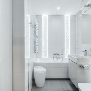 Mała łazienka z wanną w białym kolorze, który optycznie powiększa wnętrze. Przestrzeń powiększa też duże lustro i błyszczące płytki. Projekt: Justyna Mojżyk. Zdjęcie: Monika Filipiuk-Obałek