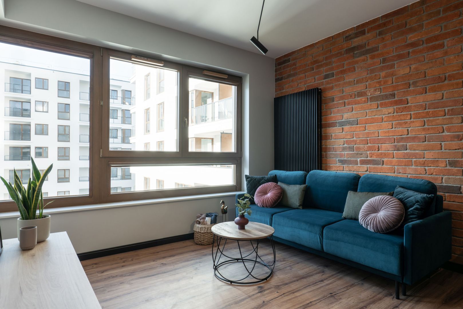 Niebieska kanapa w salonie pięknie prezentuje się na tle ceglanej ściany. Projekt i zdjęcia: KODO Projekty i Realizacje Wnętrz