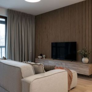 Ściana za telewizorem wykończona jest pionowymi, drewnianymi lamelami. Projekt i zdjęcie: KODO Projekty i Realizacje Wnętrz
