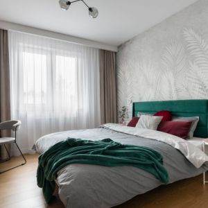 Ściana za łóżkiem w sypialni wykończona jest jasną tapetą w liście palmy. Projekt: Karolina Poniatowska, KOKA pracownia. Fot. Mikołaj Dąbrowski
